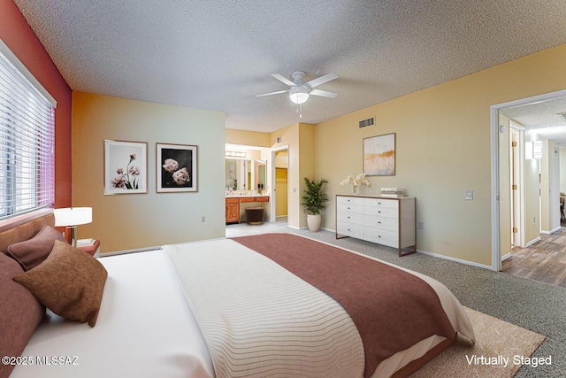 bedroom with ensuite bathroom, carpet floors, ceiling fan, and a textured ceiling