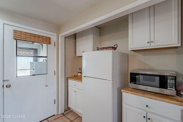 kitchen featuring white refrigerator, light tile patterned floors, white cabinets, and wood counters