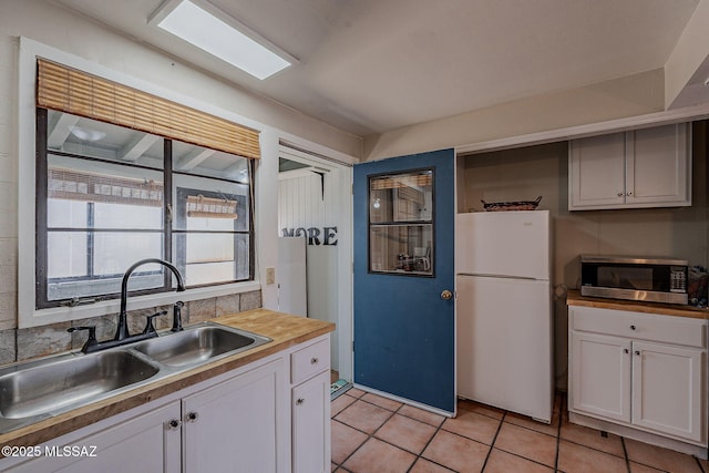 kitchen with light tile patterned flooring, sink, white cabinets, wooden counters, and white refrigerator