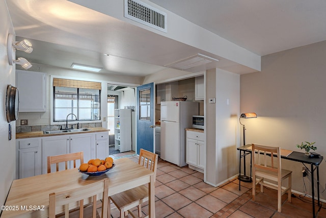 kitchen featuring white refrigerator, light tile patterned floors, sink, and white cabinets