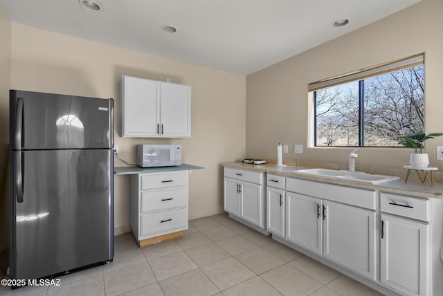 kitchen with fridge, sink, light tile patterned floors, and white cabinets