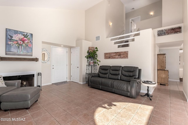 living area featuring baseboards, visible vents, tile patterned floors, a high ceiling, and a fireplace