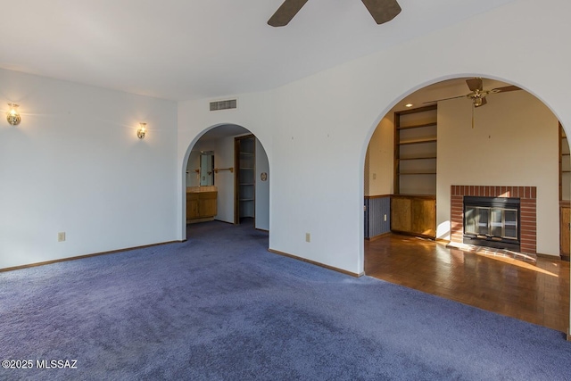 unfurnished living room featuring built in features, a brick fireplace, carpet, and ceiling fan