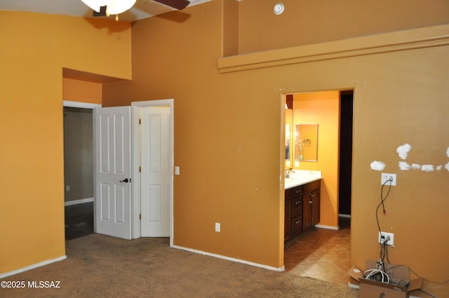 unfurnished bedroom with a sink, ensuite bathroom, a towering ceiling, baseboards, and carpet floors
