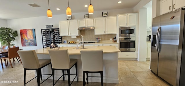 kitchen with appliances with stainless steel finishes, pendant lighting, white cabinetry, backsplash, and a kitchen island with sink