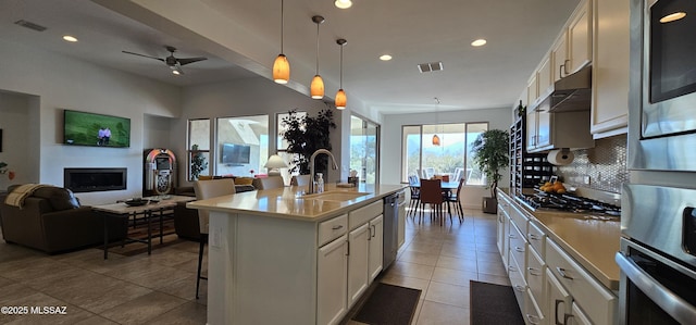 kitchen with pendant lighting, sink, stainless steel appliances, an island with sink, and white cabinets