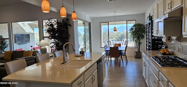 kitchen featuring an island with sink, sink, decorative backsplash, hanging light fixtures, and stainless steel appliances