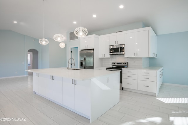 kitchen featuring arched walkways, stainless steel appliances, a sink, light countertops, and decorative backsplash