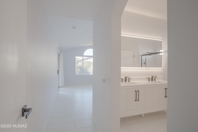 hallway with arched walkways, baseboards, vaulted ceiling, and light tile patterned floors