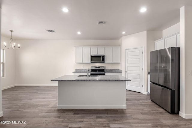 kitchen with white cabinetry, a kitchen island with sink, light stone countertops, and appliances with stainless steel finishes