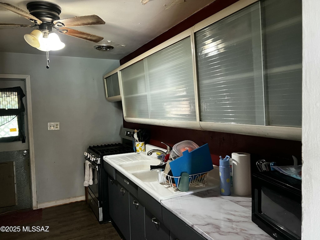 kitchen with dark wood-type flooring, gas stove, and ceiling fan