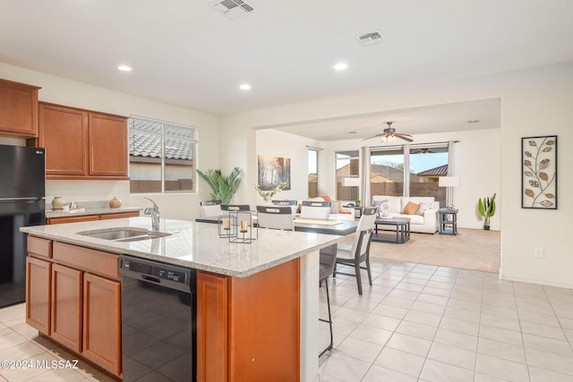 kitchen featuring sink, light stone counters, a center island with sink, light tile patterned floors, and black appliances