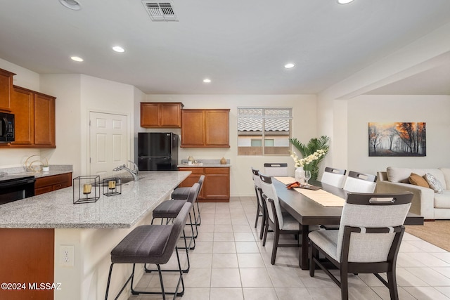 kitchen with a breakfast bar, light stone counters, light tile patterned floors, an island with sink, and black appliances