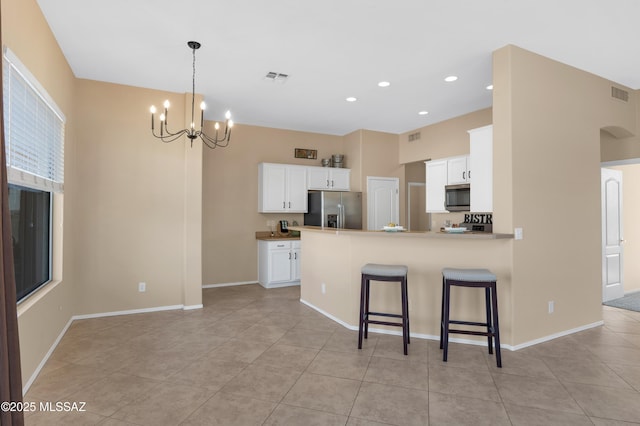 kitchen featuring a kitchen breakfast bar, stainless steel appliances, white cabinets, kitchen peninsula, and a chandelier