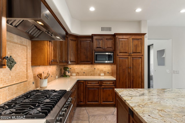 kitchen featuring tasteful backsplash, appliances with stainless steel finishes, light stone counters, and wall chimney range hood