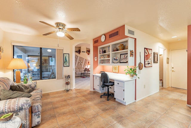 office space featuring ceiling fan, built in desk, and a textured ceiling