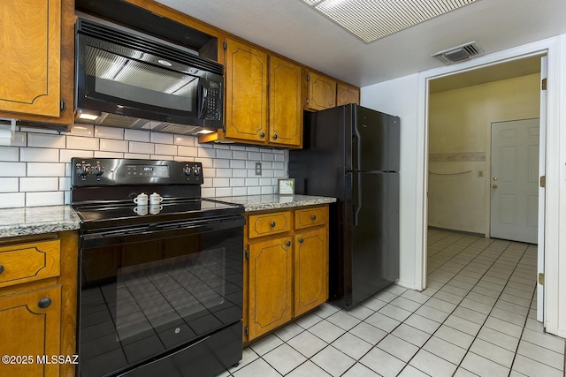 kitchen featuring backsplash, light tile patterned flooring, light stone counters, and black appliances