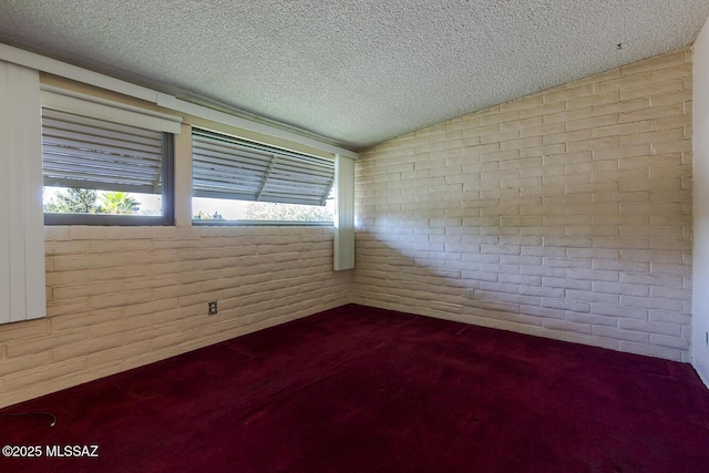 carpeted spare room with a textured ceiling and brick wall