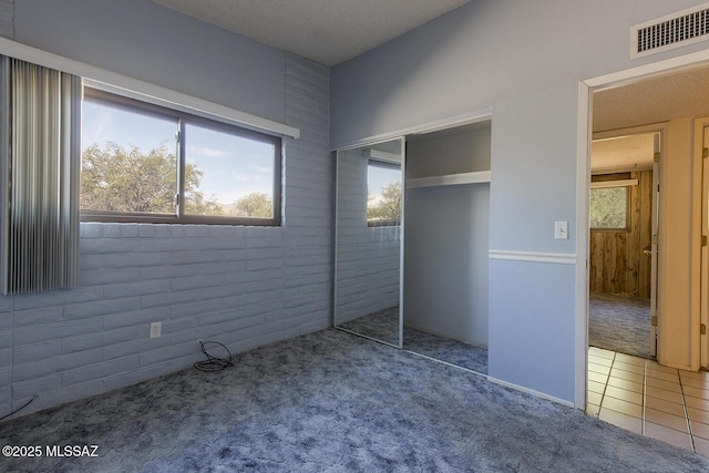 unfurnished bedroom featuring brick wall, carpet, and a closet