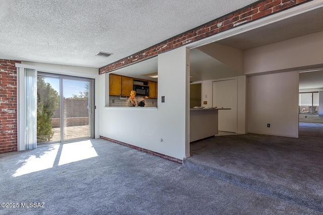 unfurnished living room with brick wall, a textured ceiling, and carpet flooring