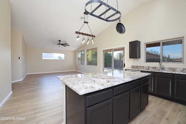 kitchen with a sink, high vaulted ceiling, a center island, light stone countertops, and light wood-style floors