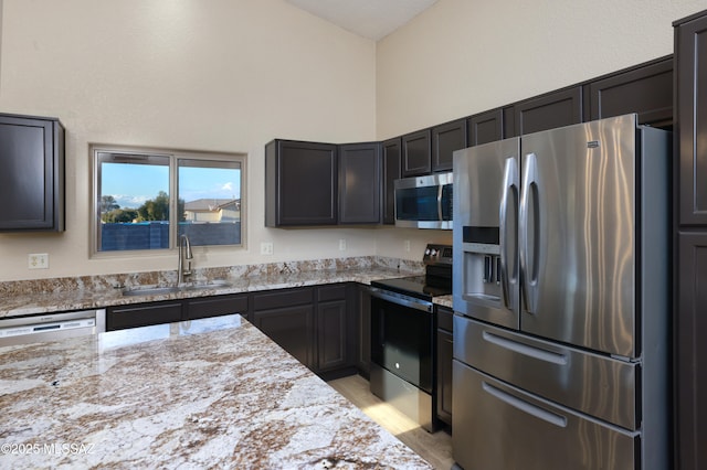 kitchen with sink, light hardwood / wood-style flooring, appliances with stainless steel finishes, a towering ceiling, and light stone countertops