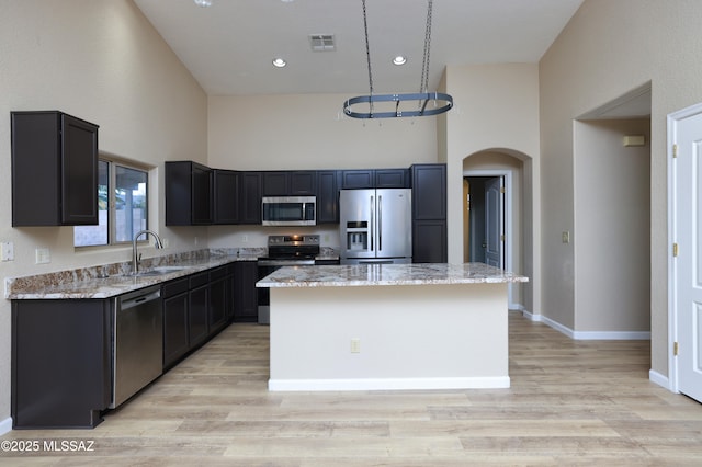 kitchen featuring sink, a center island, a towering ceiling, stainless steel appliances, and light stone countertops