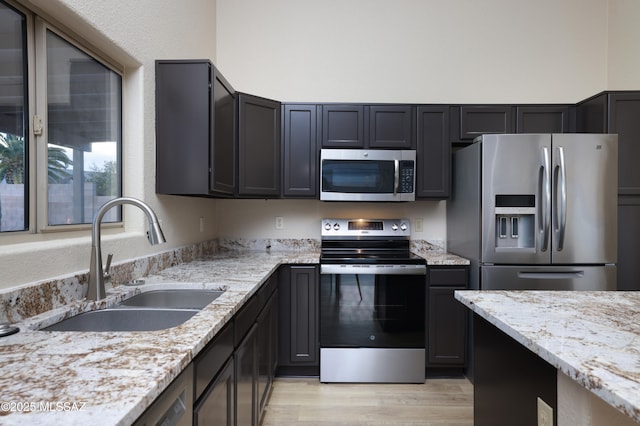 kitchen featuring light stone counters, appliances with stainless steel finishes, sink, and light hardwood / wood-style flooring