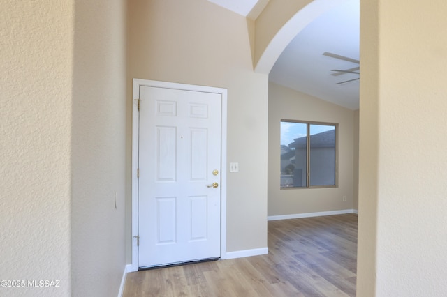 foyer with lofted ceiling, a ceiling fan, baseboards, wood finished floors, and arched walkways