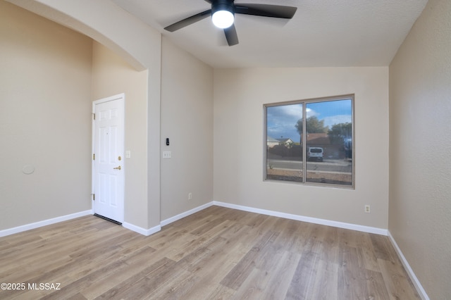 empty room with light wood-type flooring, baseboards, a ceiling fan, and arched walkways