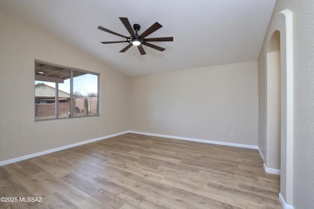 empty room with baseboards, light wood-style floors, ceiling fan, and vaulted ceiling