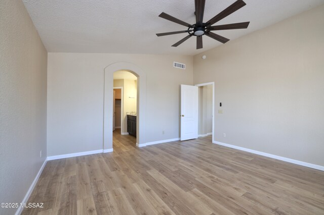 unfurnished room featuring visible vents, vaulted ceiling, ceiling fan, arched walkways, and light wood-style floors