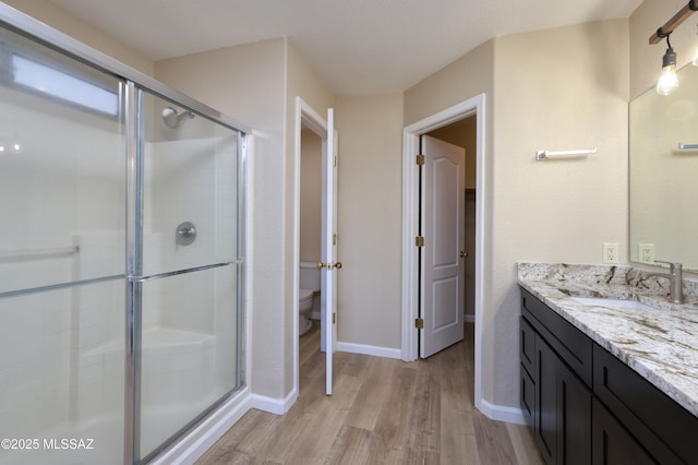 bathroom with toilet, wood finished floors, vanity, a stall shower, and baseboards
