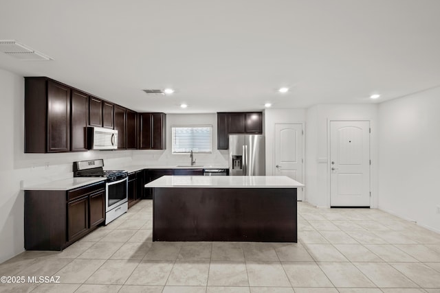 kitchen featuring sink, light tile patterned floors, appliances with stainless steel finishes, dark brown cabinets, and a kitchen island