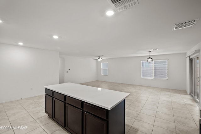 kitchen featuring light tile patterned flooring, hanging light fixtures, a center island, ceiling fan, and dark brown cabinets