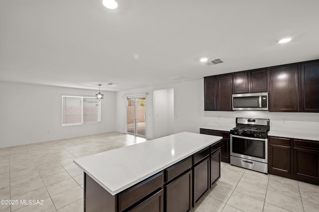 kitchen featuring light tile patterned floors, appliances with stainless steel finishes, dark brown cabinetry, a kitchen island, and decorative light fixtures