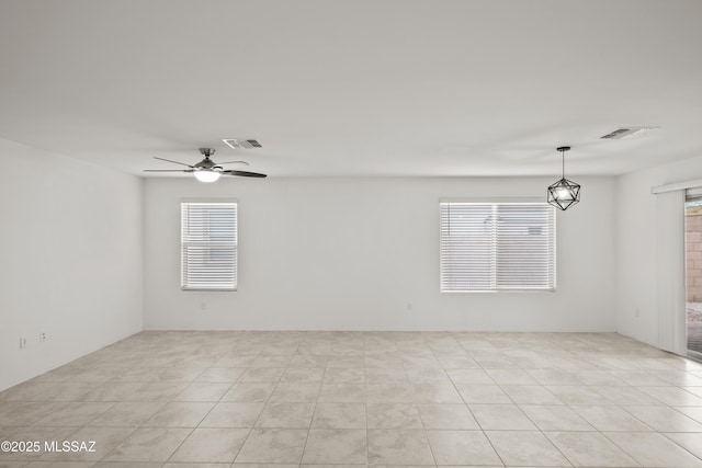 tiled spare room featuring ceiling fan with notable chandelier