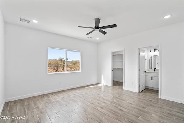 unfurnished bedroom with a walk in closet, ceiling fan, light hardwood / wood-style floors, ensuite bath, and a closet