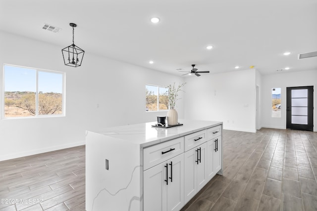 kitchen featuring a kitchen island, white cabinetry, light stone countertops, and pendant lighting