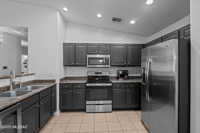 kitchen with dark countertops, a sink, lofted ceiling, appliances with stainless steel finishes, and visible vents