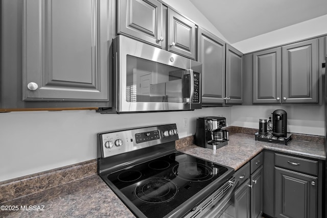 kitchen featuring dark countertops, vaulted ceiling, stainless steel appliances, and gray cabinetry
