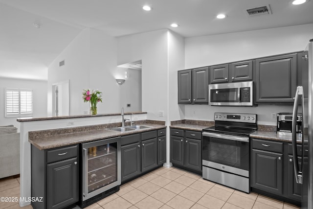 kitchen featuring dark countertops, a sink, stainless steel appliances, a peninsula, and wine cooler
