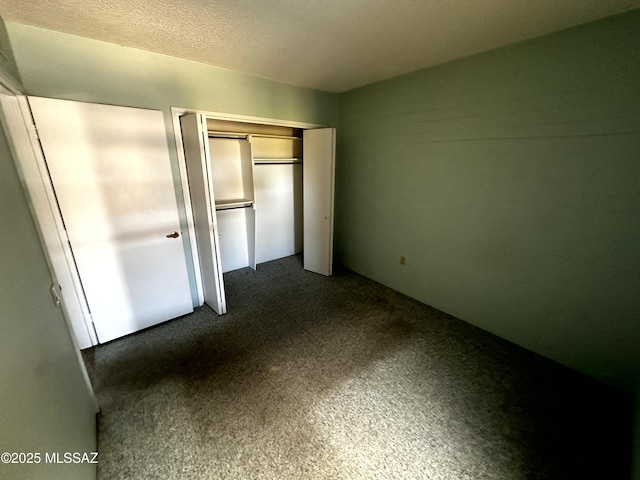 unfurnished bedroom featuring a textured ceiling, a closet, and dark colored carpet