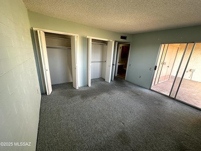 unfurnished bedroom featuring multiple closets, dark colored carpet, and a textured ceiling