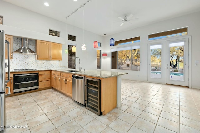 kitchen featuring wine cooler, sink, pendant lighting, stainless steel appliances, and wall chimney range hood