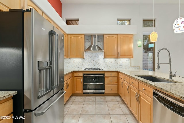 kitchen with sink, light stone counters, pendant lighting, stainless steel appliances, and wall chimney range hood