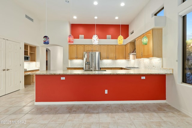 kitchen with hanging light fixtures, a towering ceiling, stainless steel appliances, light stone counters, and kitchen peninsula