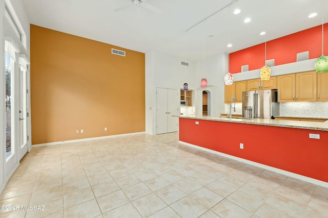 kitchen with sink, tasteful backsplash, hanging light fixtures, high quality fridge, and a towering ceiling