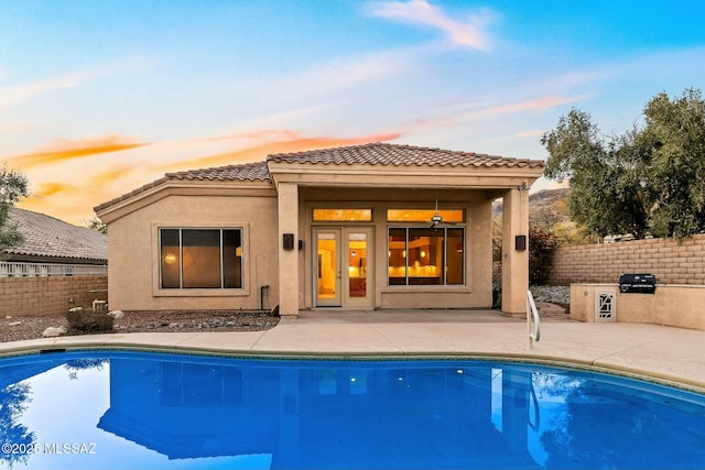 back house at dusk with a fenced in pool, a patio area, and exterior kitchen