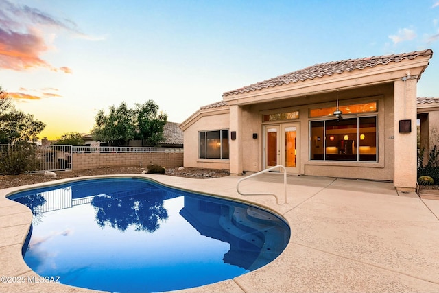 pool at dusk featuring a patio, ceiling fan, and french doors